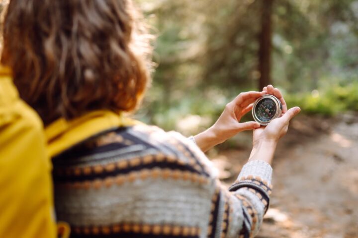 Ilustračný stock: turista drží kompas v ruke vo vonkajšom prostredí, mobilný telefón a batoh v blízkosti, bez čitateľného textu, bez loga